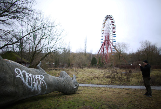 A man takes photograph of a fibreglass model of a dinosaur at the abandoned Plaenterwald amusement park in Berlin January 5, 2013. Berlin is littered with relics of its communist past, and one of the eeriest is the Spreepark, where the remains of what was once East Germany's only amusement park still stands. REUTERS/stringer (GERMANY - Tags: SOCIETY CITYSPACE) - RTR3C4IW